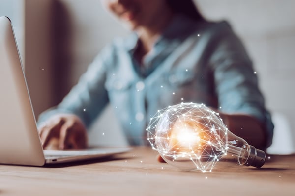 Premier plan : ampoule avec structure digitale autour / second plan : personne sur son ordinateur